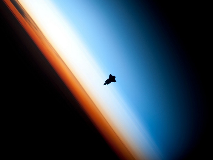 Space shuttle silhouette against Earth's atmosphere