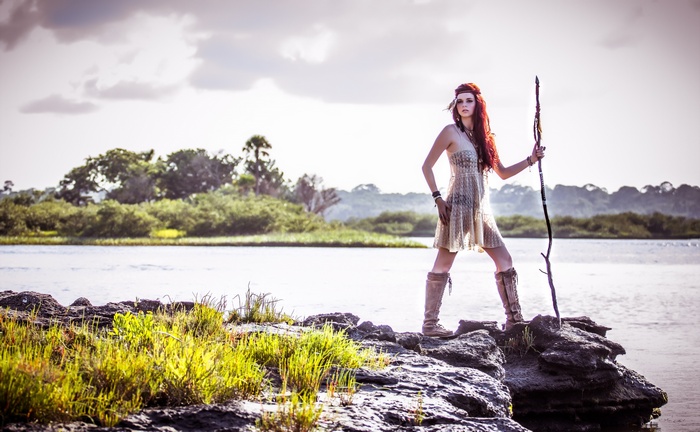 Redhead woman with staff on rocks by water