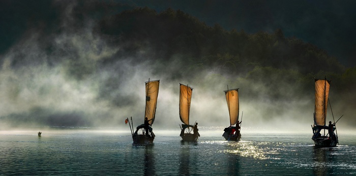 Boats sailing on a misty river with forested hills