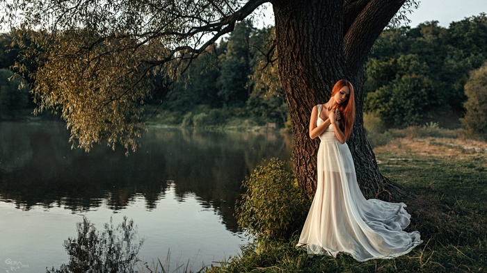 Woman in white dress by a tree near a lake