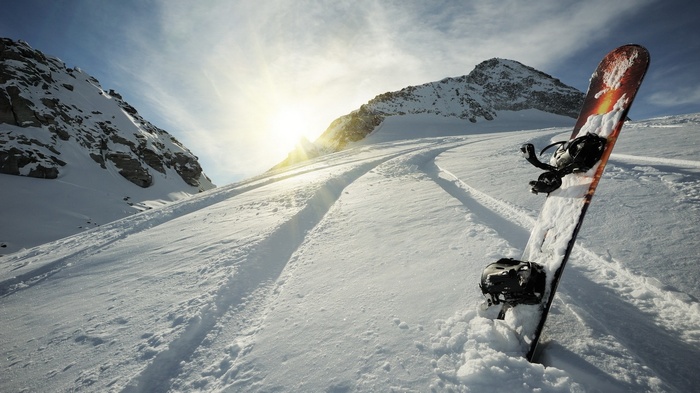 Snowboard leaning in snowy mountain landscape with sun