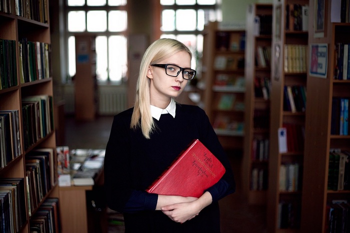Woman with glasses holding a red book in a library