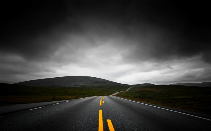 Asphalt road with yellow lines under dark clouds