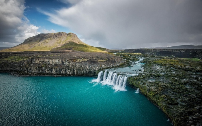 Turquoise waterfall cascading over lava cliffs in Iceland