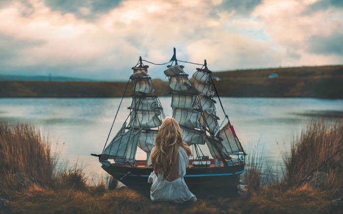 Woman in white dress with model sailing ship by lake