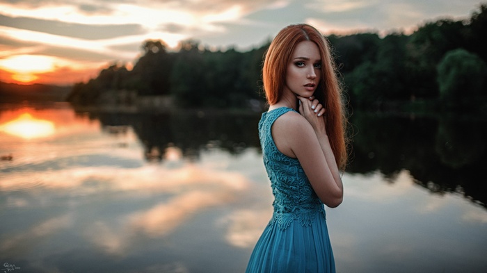 Redhead woman in blue dress by lake at sunset