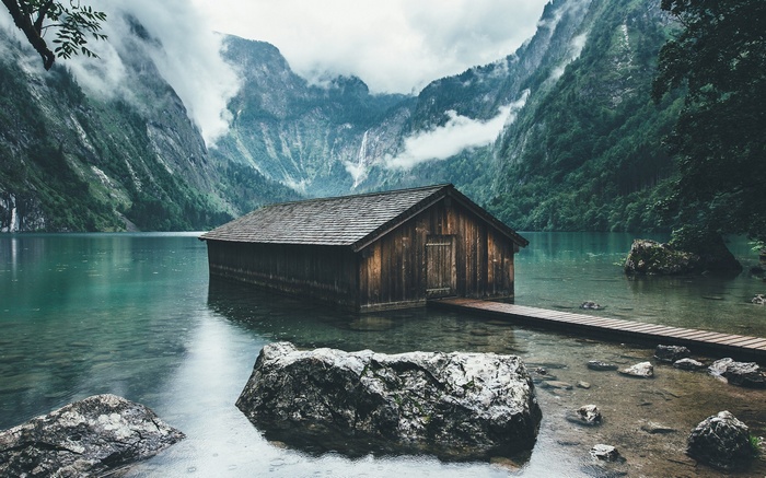 Wooden cabin on a lake with misty mountains