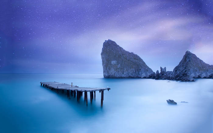 Long exposure of a pier and rocks under a starry sky