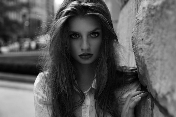 Monochrome portrait of a woman leaning against a stone wall