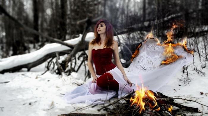 Woman in red corset sitting by a fire in a snowy forest