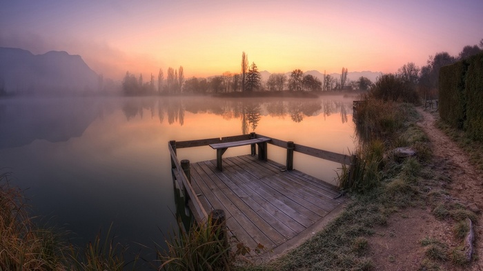 Wooden dock on a misty lake at sunrise with mountains