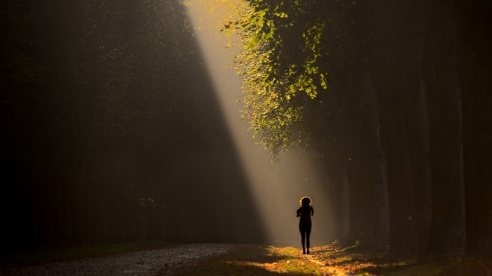 Woman running on a path in a sunlit forest
