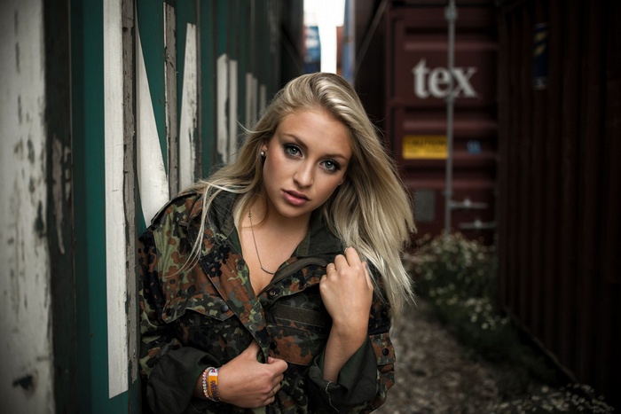 Woman in camouflage jacket leaning against shipping containers
