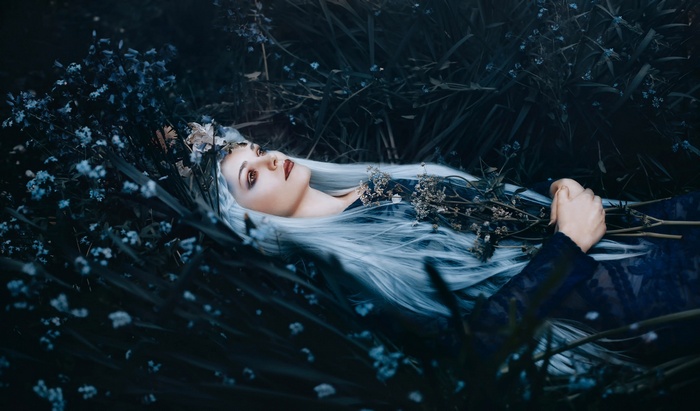 Woman with white hair lying in dark flowers