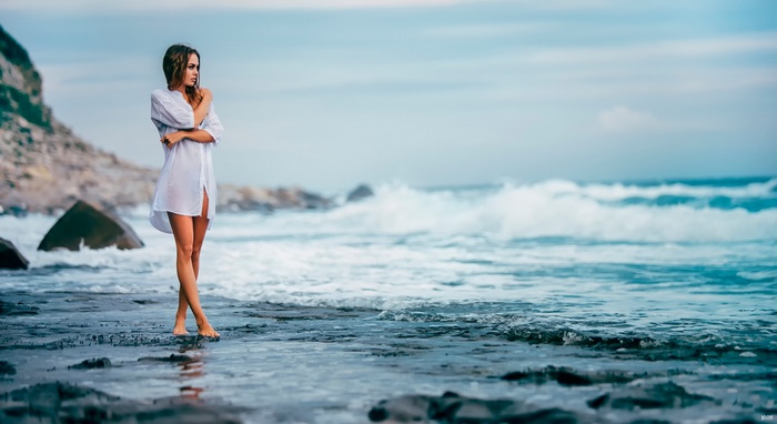 Woman in white shirt on a rocky beach with waves