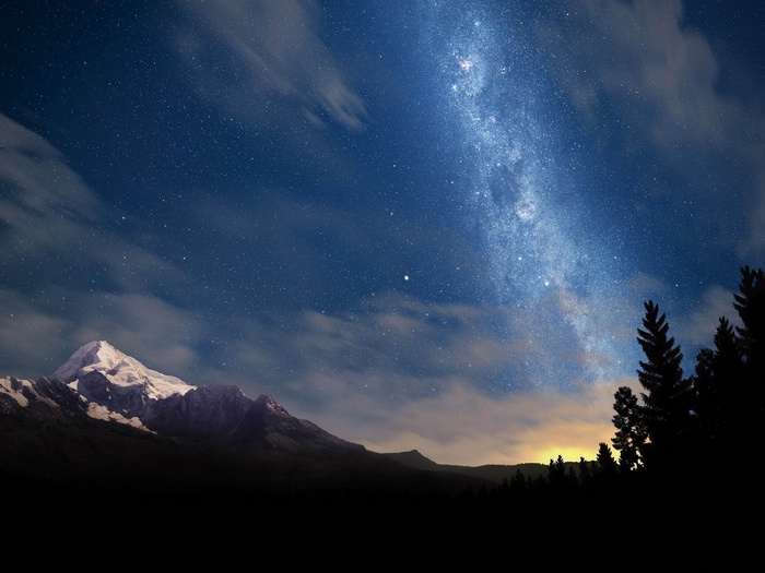 Milky Way over snow-capped mountains and forest