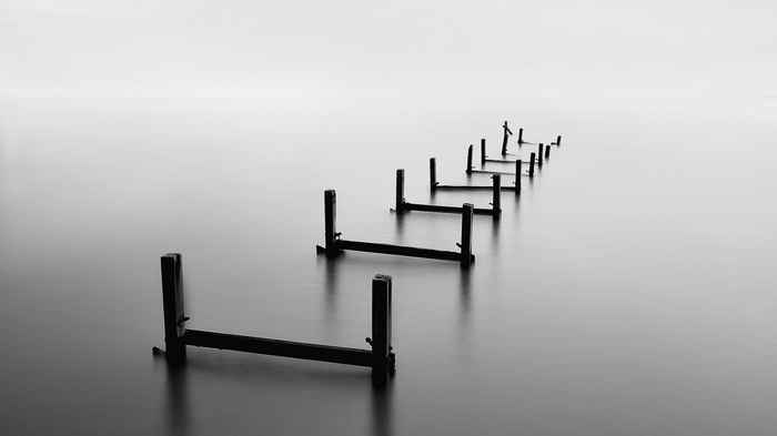 Monochrome long exposure of wooden pier ruins in calm water
