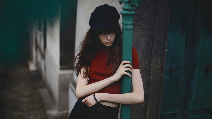 Woman in red shirt and black hat leaning on pole