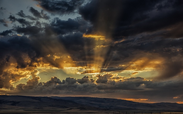 Sun rays breaking through dark clouds over hills