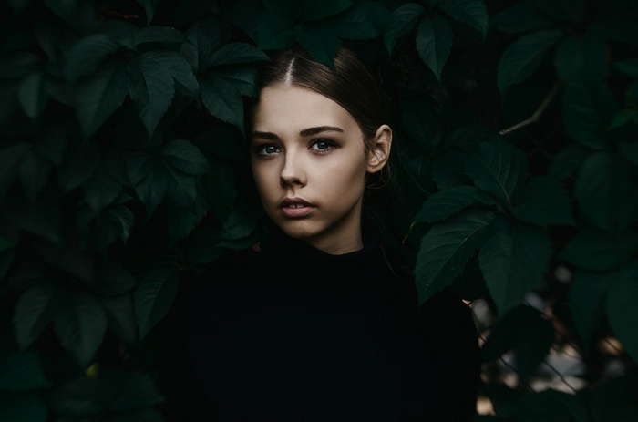 Portrait of a young woman among dark green leaves
