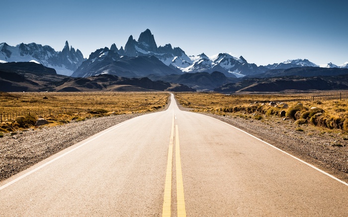 Road leading to snowy mountain peaks under a clear sky