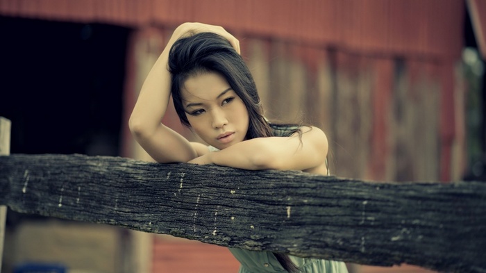 Woman with hands in dark hair leaning on a wooden fence