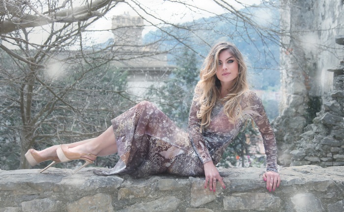 Woman in a patterned dress sitting on a stone wall