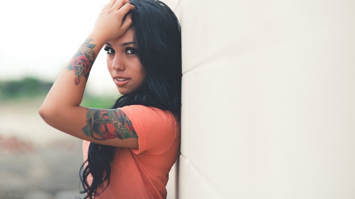 Woman with tattoos leaning against a wall