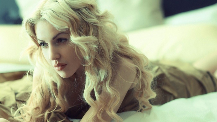 Woman with blonde curly hair lying on bed