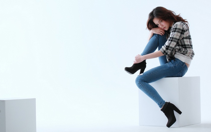Woman in plaid shirt and jeans sitting on cube