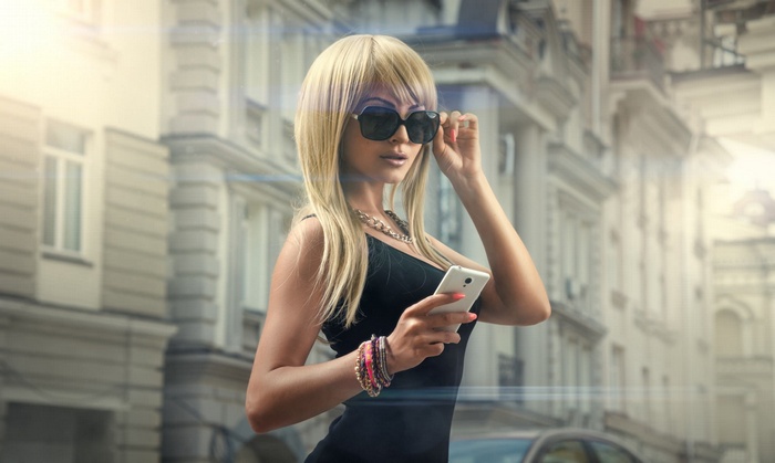 Woman with blonde hair and sunglasses holding a cellphone
