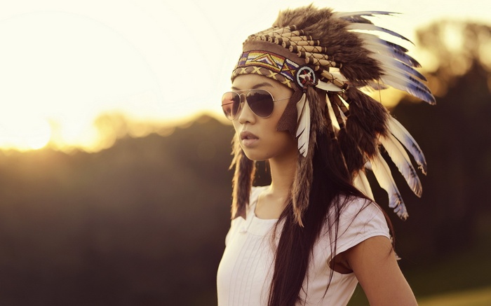 Asian woman wearing Native American headdress and sunglasses