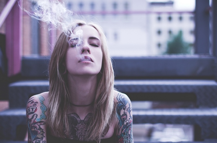 Woman with tattoos smoking with eyes closed