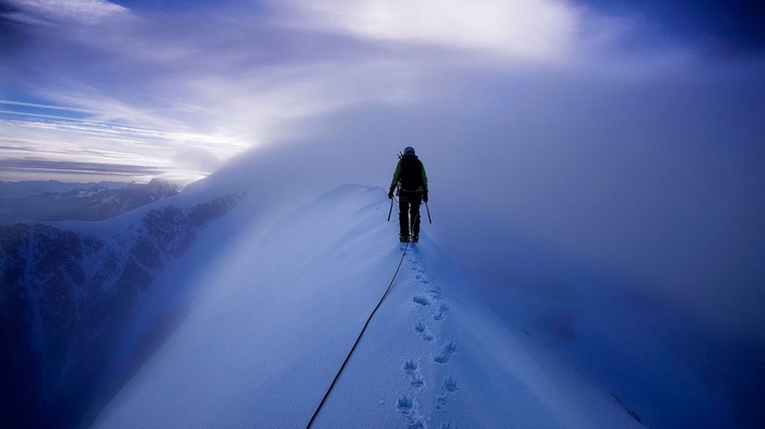 Climber on a snowy mountain ridge with clouds