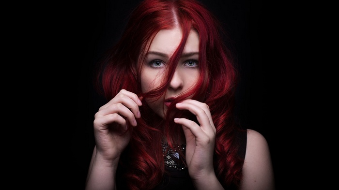 Woman with vibrant red hair against a black background