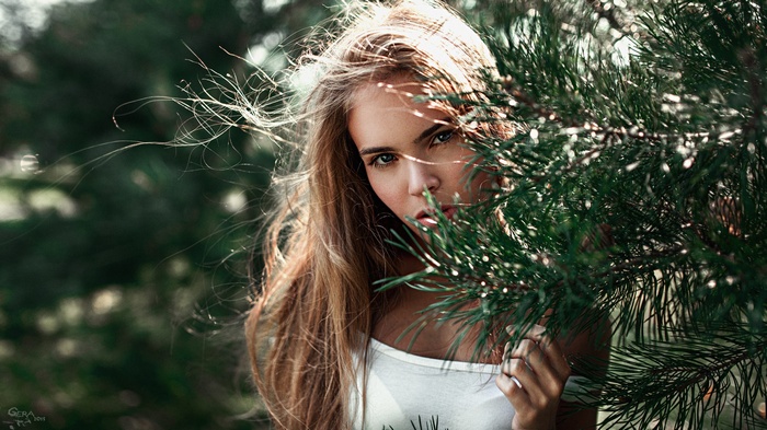 Woman with blonde hair behind pine branches