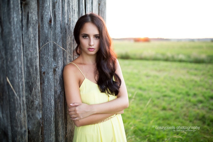 Woman in yellow dress leaning against wooden fence outdoors