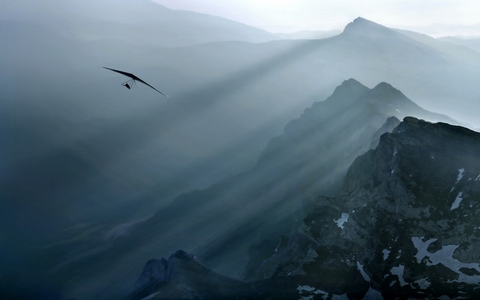 Hang glider flying through misty mountains with sun rays