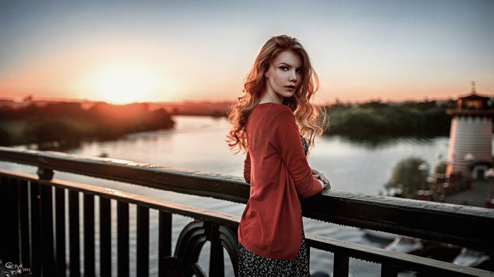 Woman with long red hair on a bridge at sunset