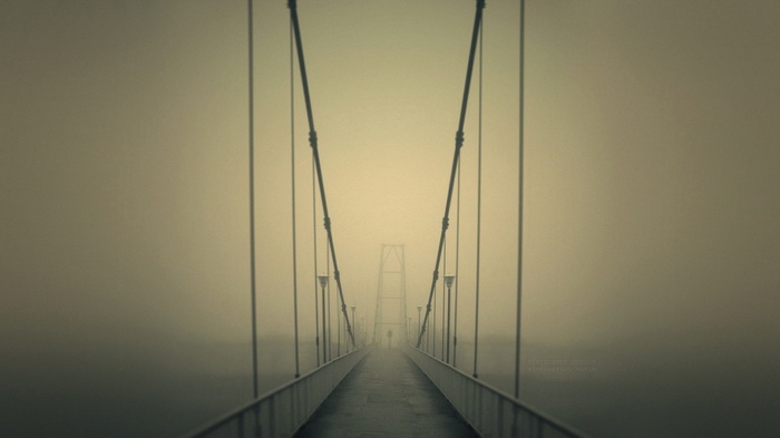 A person walks on a bridge in the mist