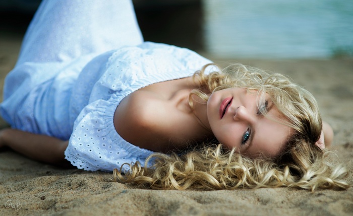Woman with blonde curly hair lying on the sand