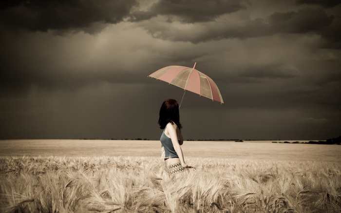 Woman with umbrella in a wheat field under storm clouds