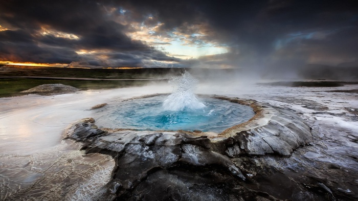 Geyser erupting in Iceland with dramatic clouds