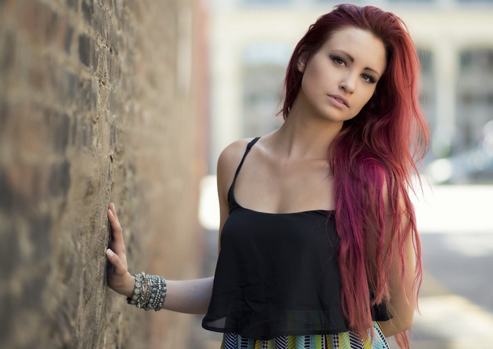 Woman with dyed hair leaning against a brick wall