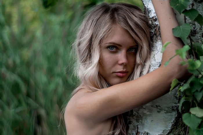 Woman with blonde hair leaning against a tree