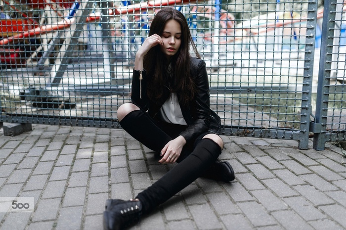 Woman in leather jacket sitting on pavement