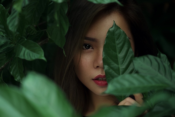 Woman peeking through green leaves