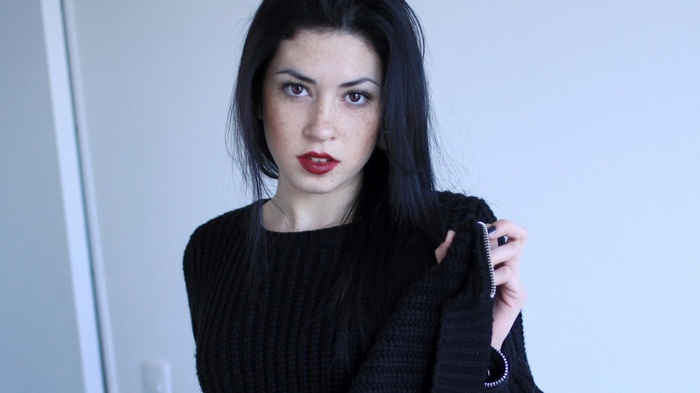Woman with black hair and freckles wearing a black sweater