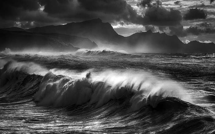 Monochrome waves crash against mountains under stormy clouds