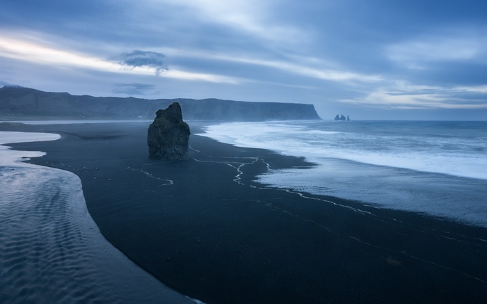 Black sand beach with rock formations and ocean waves
